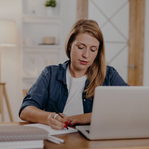 Female psychologist writing in notepad while making video call to online client in cozy office